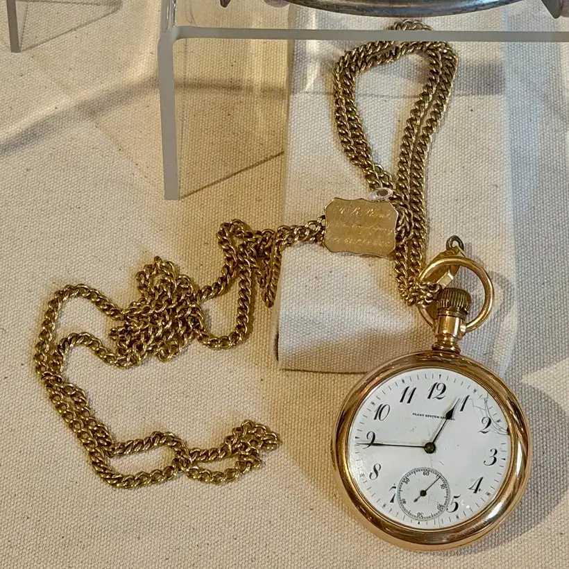 A gold railroad pocket watch with a white dial, lying on its chain